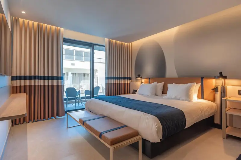 Une chambre lumineuse avec un grand lit et un accès à un balcon.