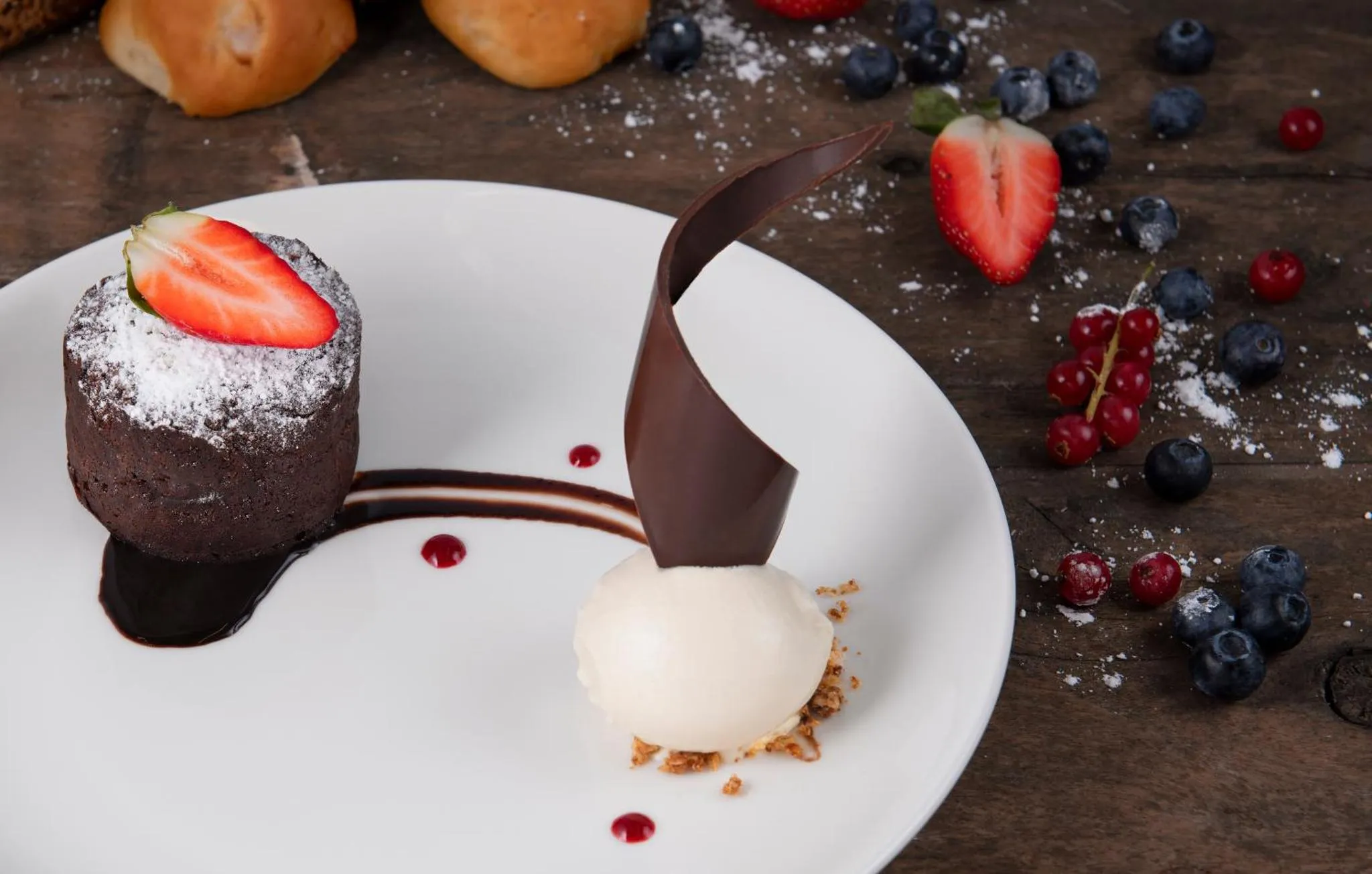 Une assiette présente un dessert au chocolat avec des fruits rouges et une crème.