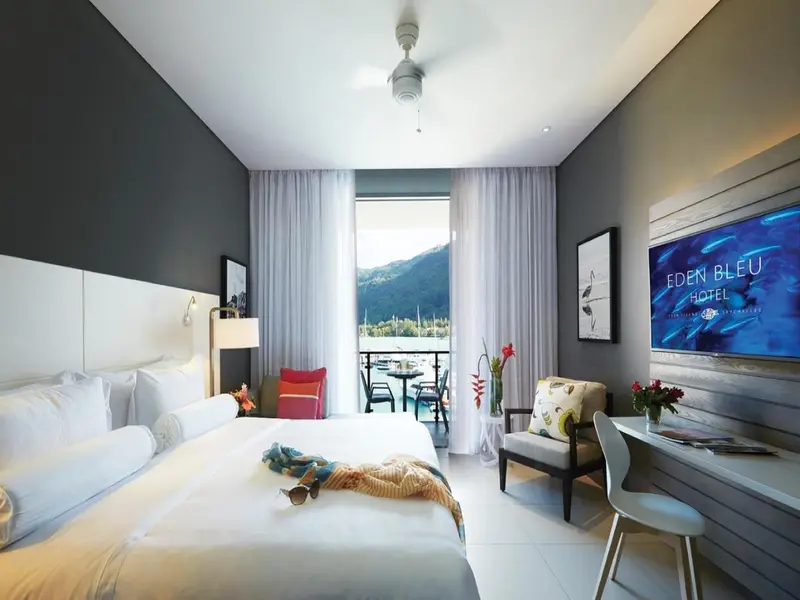 Chambre lumineuse avec un grand lit et un balcon offrant une vue sur la végétation.