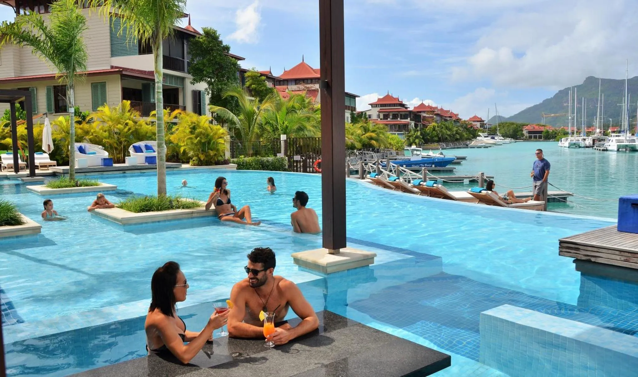 Des clients discutent autour d'un bar intégré à une piscine ensoleillée.