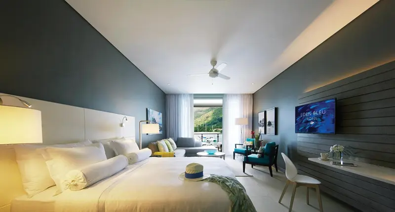 Chambre lumineuse avec un grand lit et un espace salon donnant sur une vue extérieure.