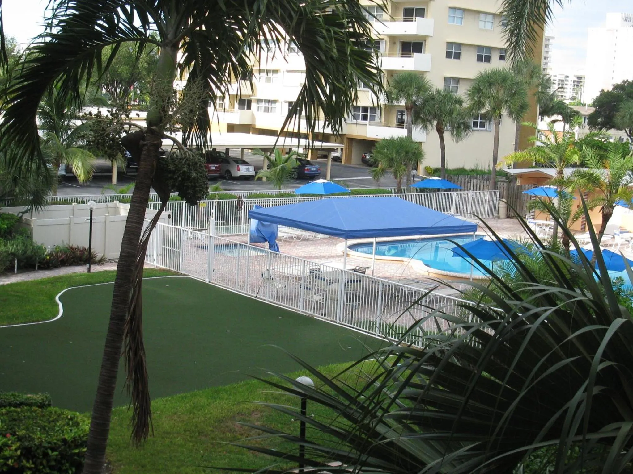 Vue d'une piscine avec des parasols bleus et une pelouse verte.