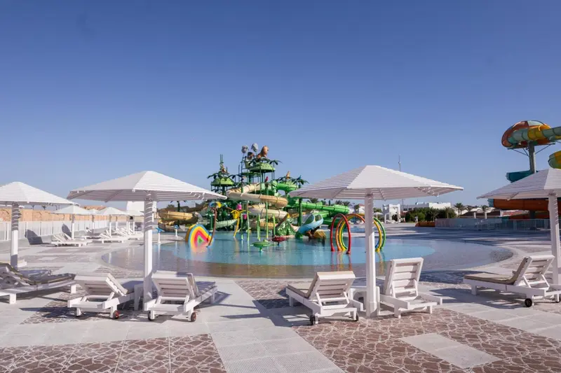 Transats blancs disposés autour d'une piscine avec un parc aquatique coloré en arrière-plan.