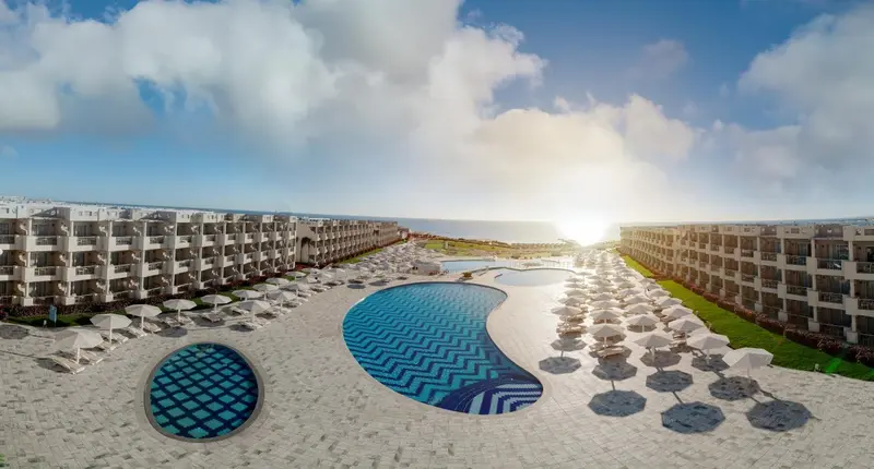 Vue aérienne d'un complexe hôtelier avec piscines et transats ensoleillés.