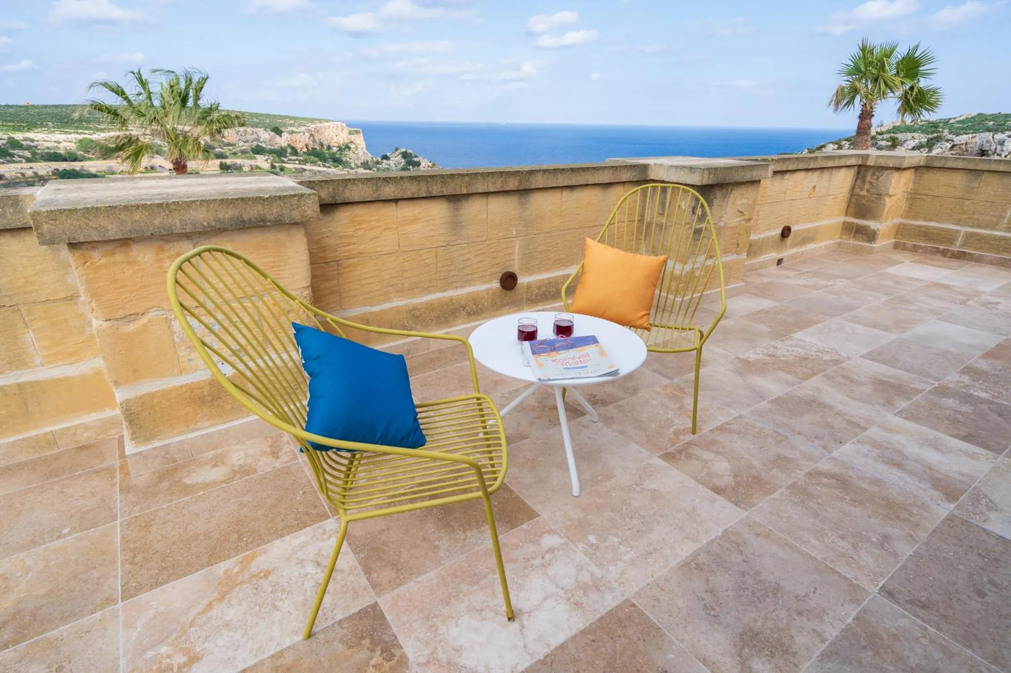 Deux fauteuils et une table basse sur une terrasse ensoleillée avec vue sur la mer.