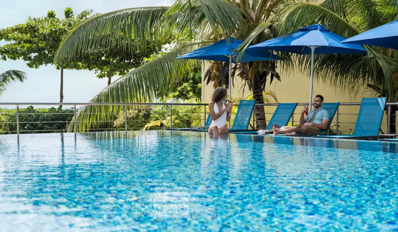 Deux personnes se détendent au bord d'une piscine turquoise avec des boissons.