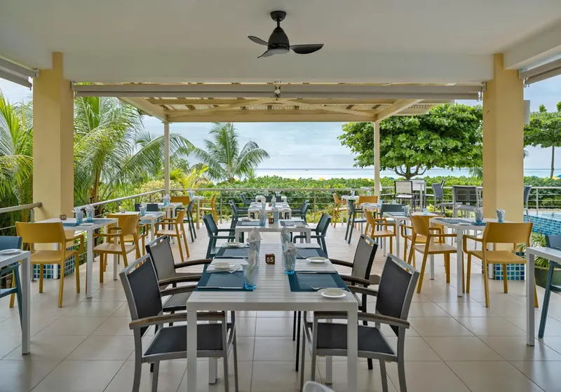 Une salle à manger extérieure avec des tables dressées face à la mer.