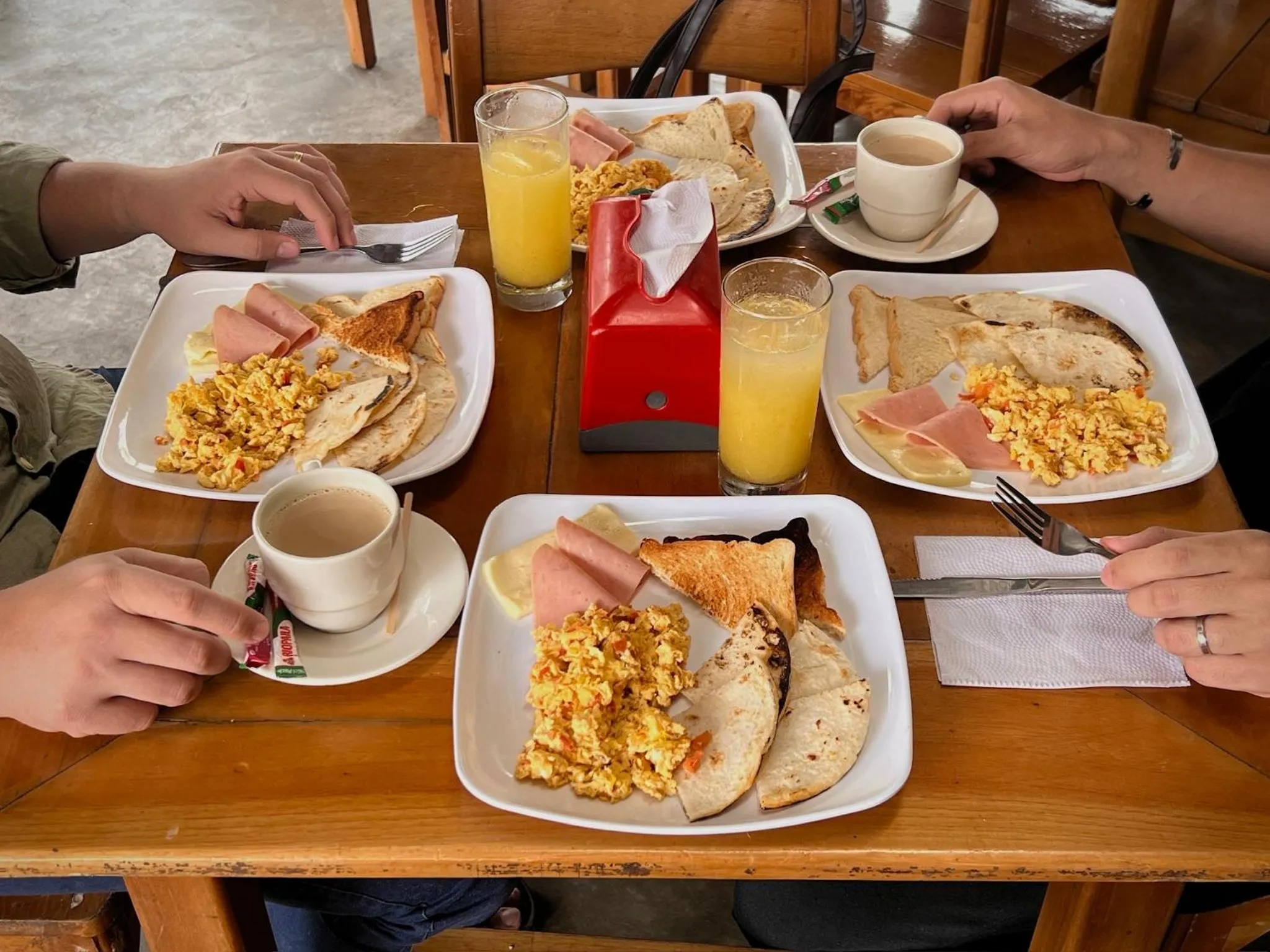 Une table en bois est servie de petits déjeuners avec des œufs brouillés, du pain et des boissons.