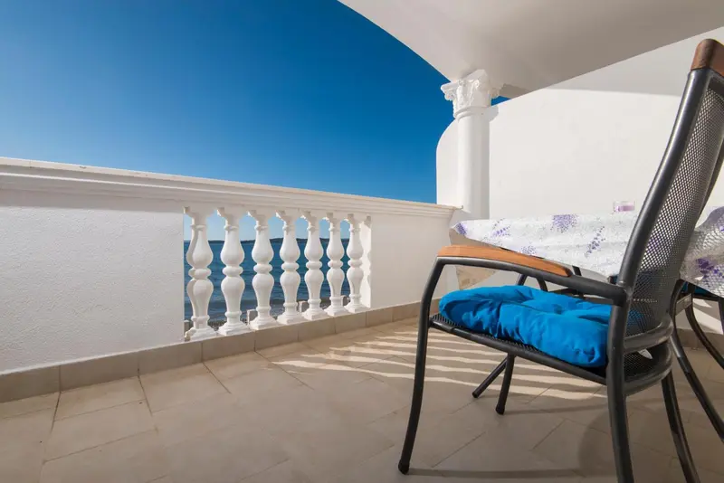 Une chaise longue sur une terrasse ensoleillée avec une rambarde blanche.