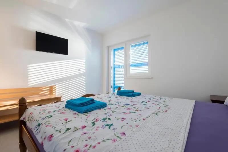 Une chambre lumineuse avec un lit recouvert d'une couverture fleurie et une télévision murale.