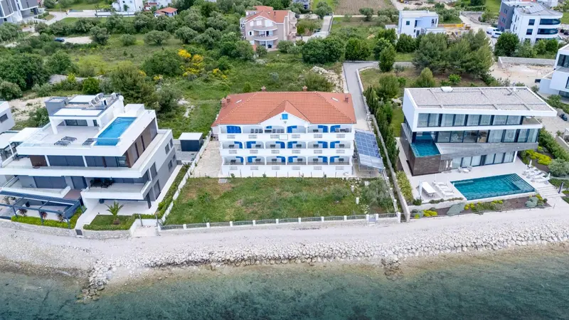 Vue aérienne de bâtiments blancs et d'une végétation luxuriante près d'une côte rocheuse.