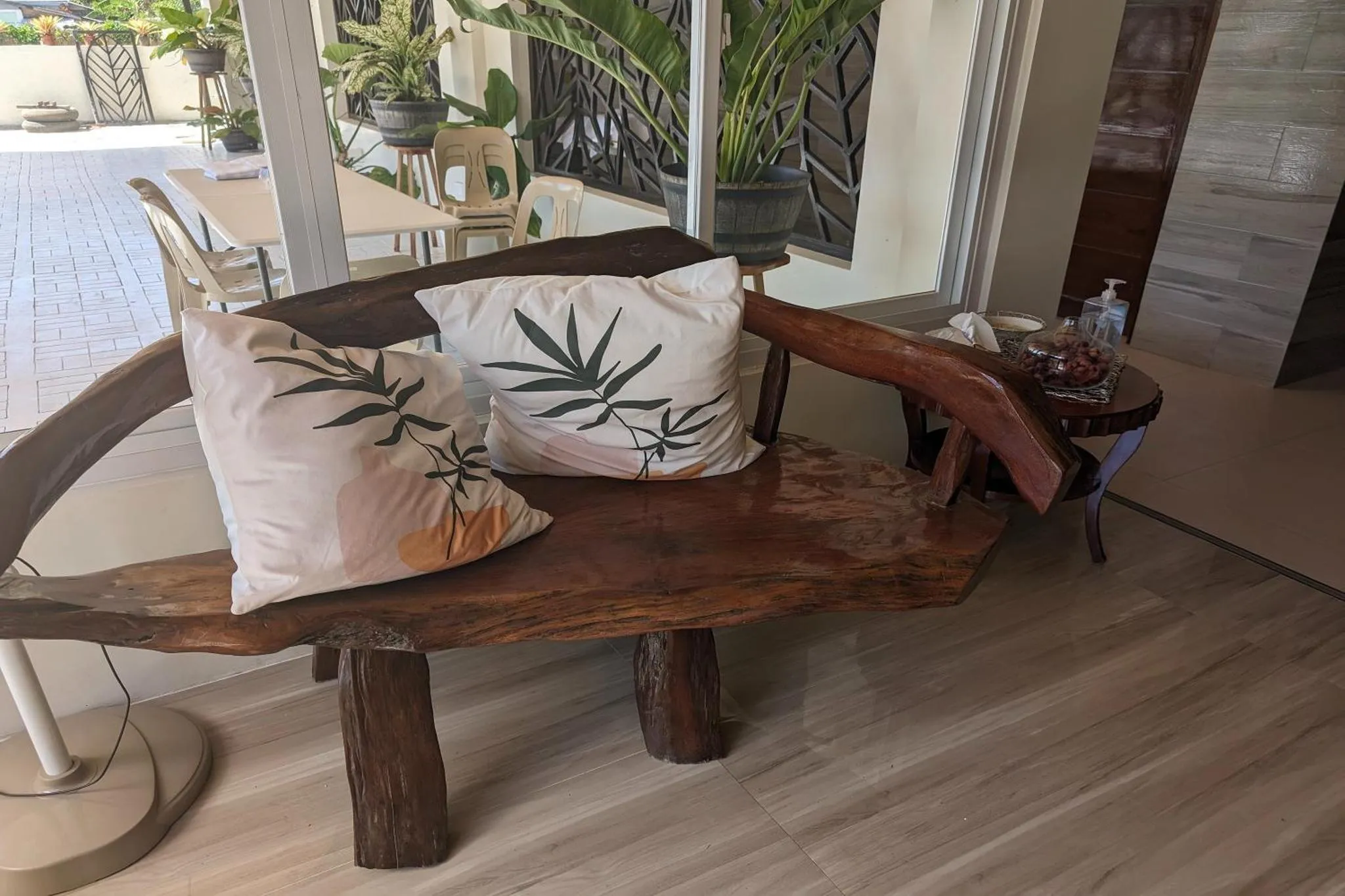 Un banc en bois sculpté avec des coussins est placé dans un espace extérieur ombragé.