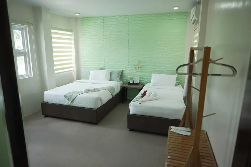 Chambre lumineuse avec deux lits simples et un mur texturé vert.