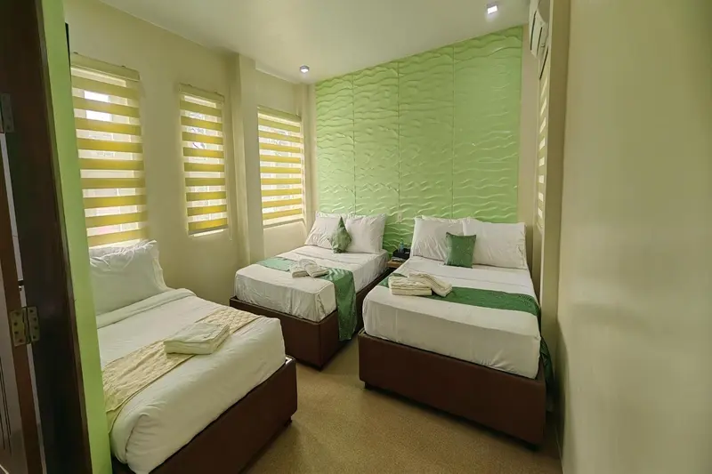 Chambre lumineuse avec trois lits simples et un mur texturé vert.