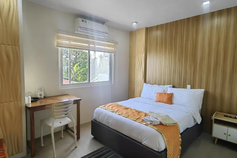 Une chambre lumineuse avec un lit double et un bureau près de la fenêtre.