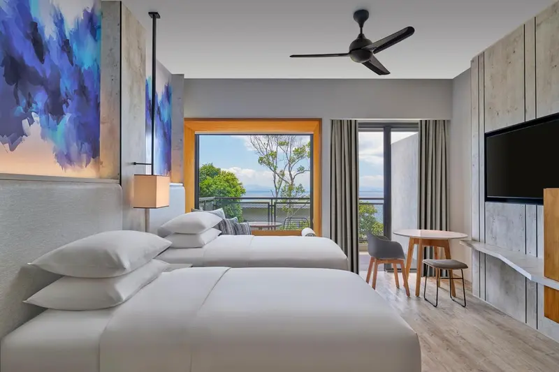 Chambre lumineuse avec deux lits et vue sur la végétation.