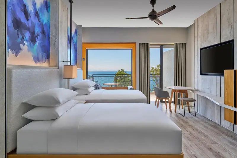 Chambre lumineuse avec deux lits et vue sur la mer par une baie vitrée.