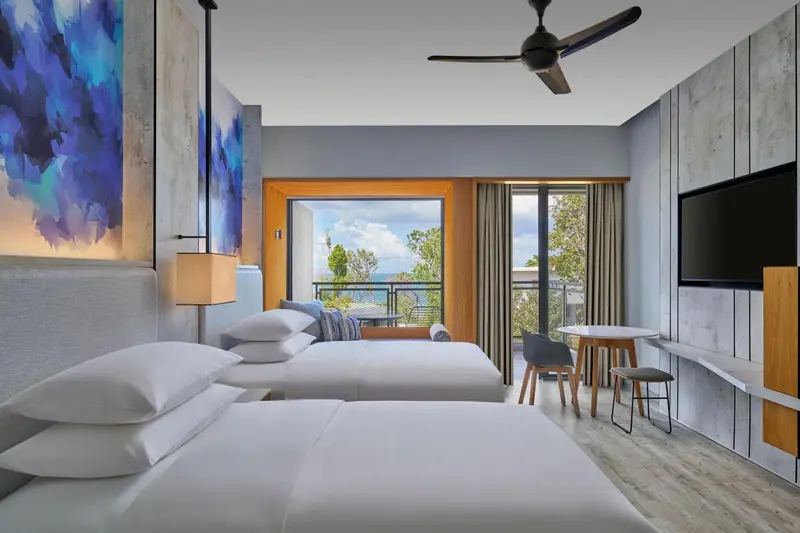 Chambre lumineuse avec deux lits et vue sur la mer.