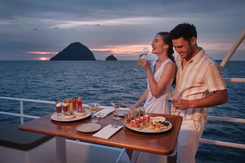 Un couple trinque au coucher du soleil depuis le pont d'un bateau.