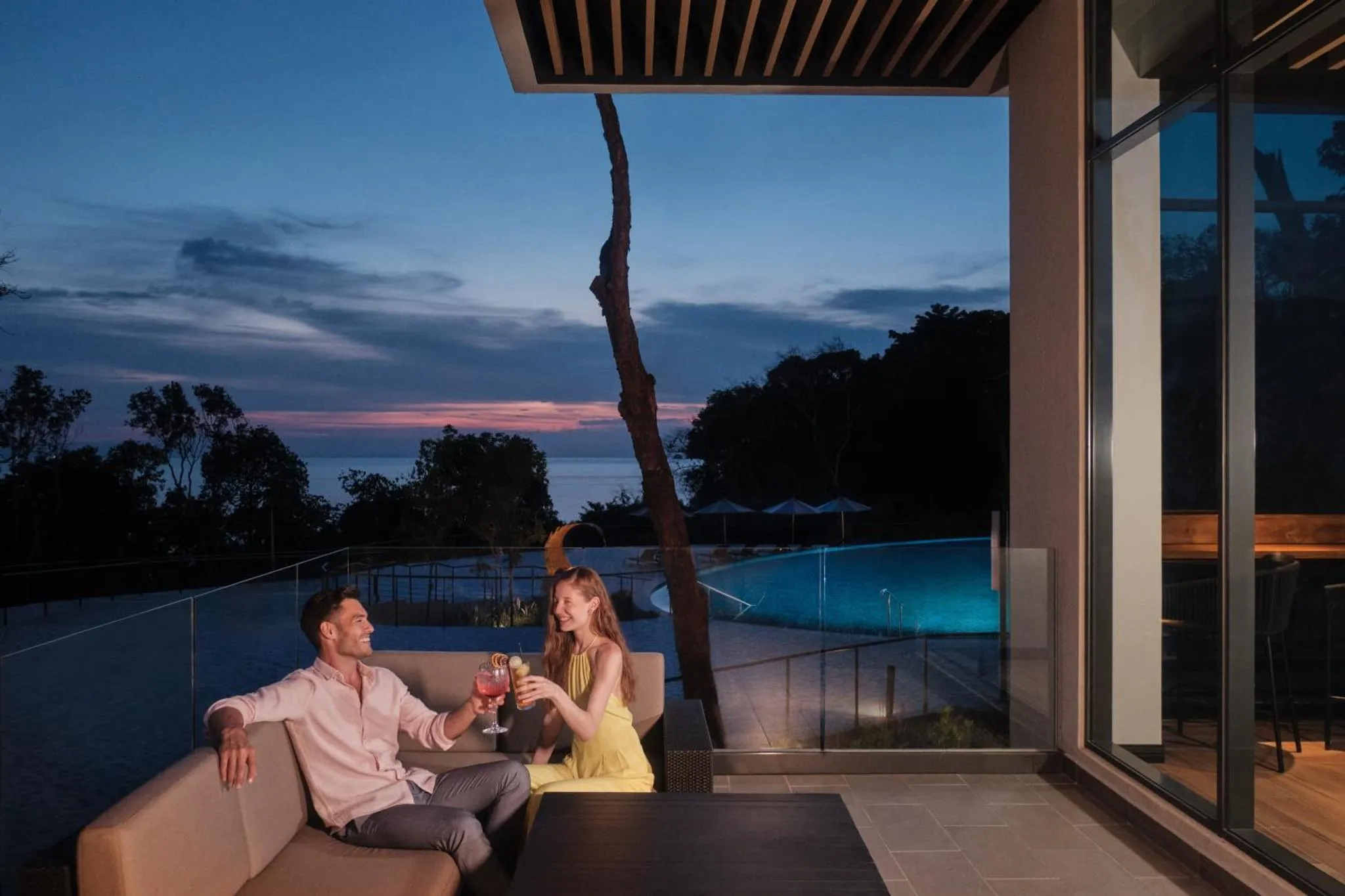Un couple profite de cocktails sur une terrasse avec vue sur la mer au crépuscule.