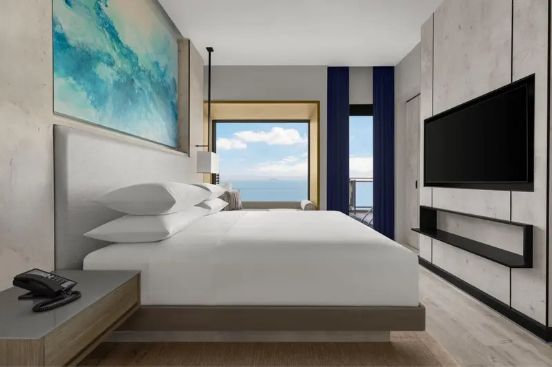 Une chambre lumineuse avec un grand lit face à une baie vitrée donnant sur la mer.