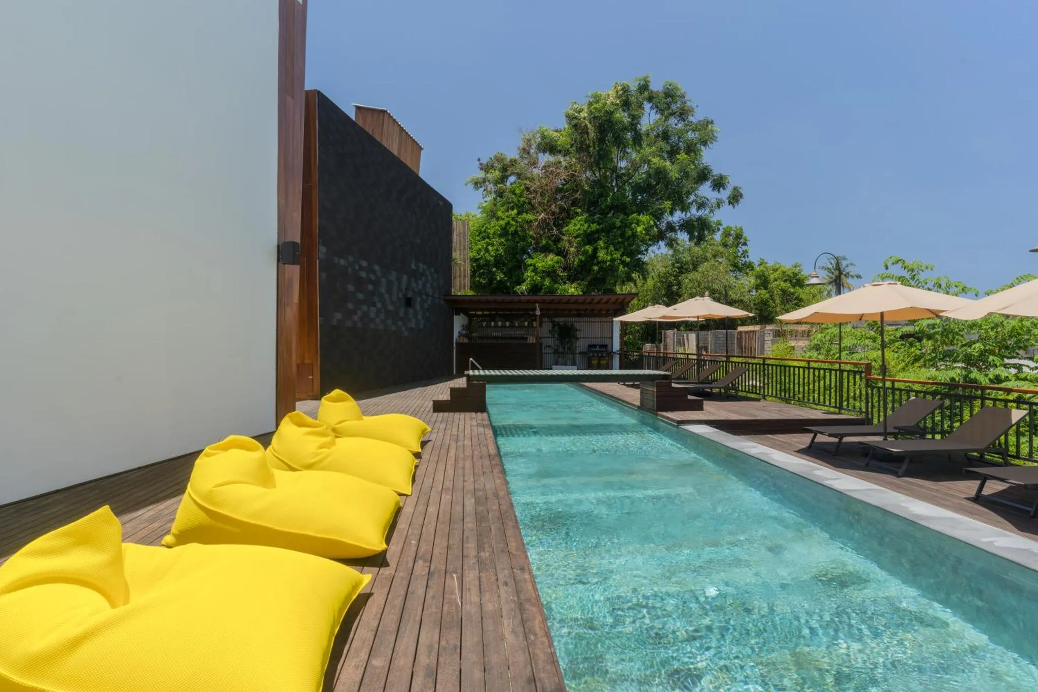 Une piscine rectangulaire bordée d'une terrasse en bois avec des transats et des fauteuils confortables.