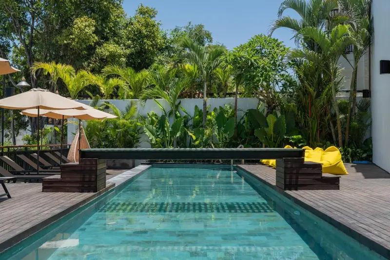 Une piscine rectangulaire bordée d'une terrasse en bois, entourée de végétation tropicale.