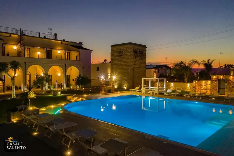 Une piscine illuminée devant un bâtiment aux arches et une tour.