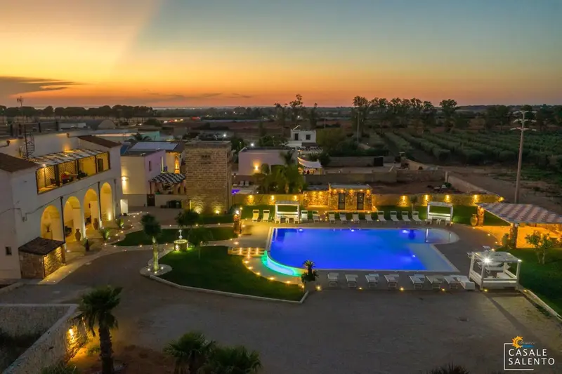 Vue aérienne d'un complexe hôtelier illuminé au crépuscule avec une piscine.