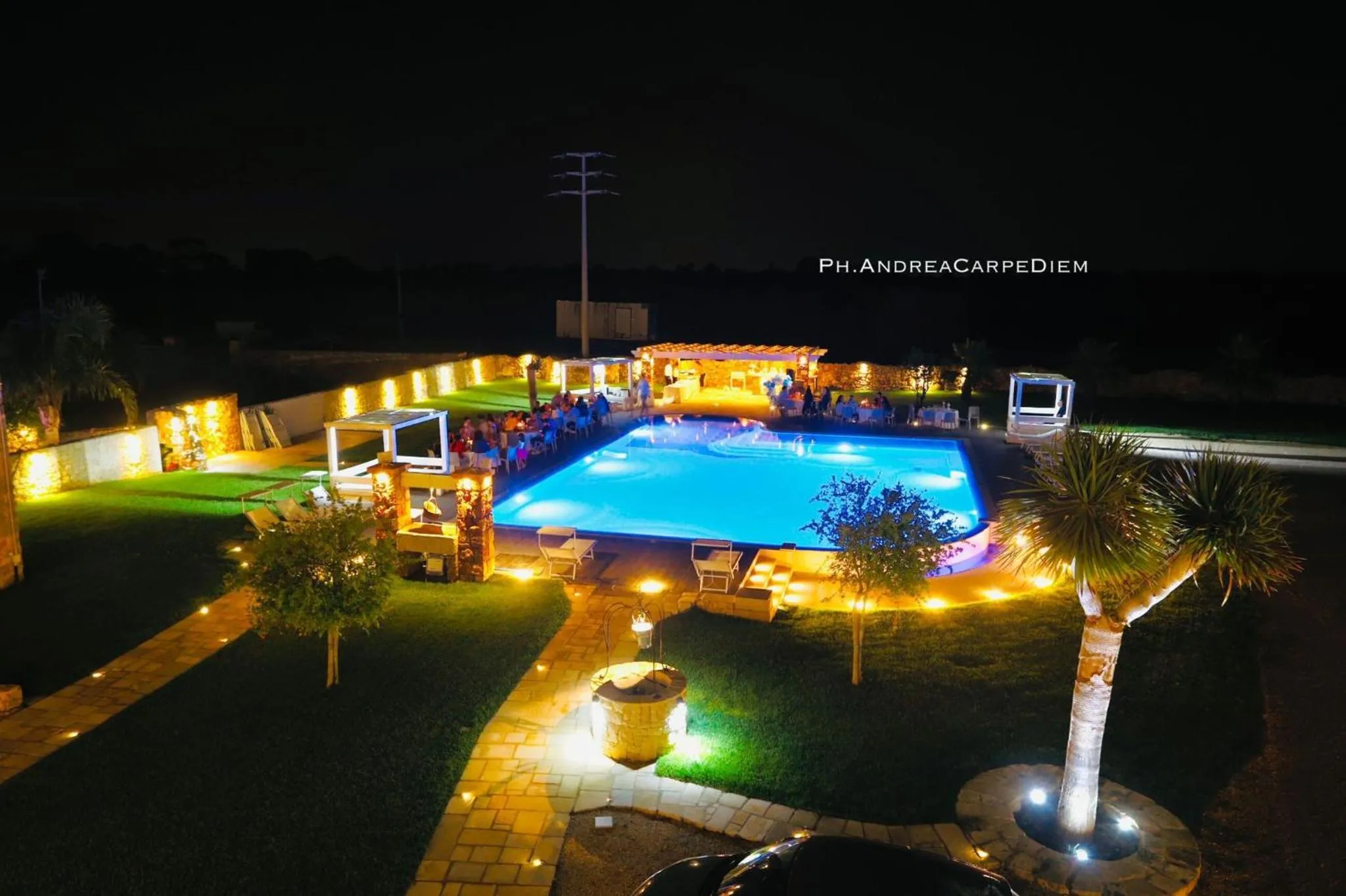 Vue nocturne d'une piscine illuminée dans un jardin tropical.