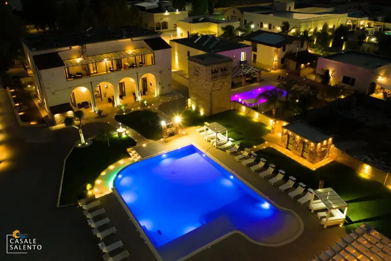 Vue aérienne nocturne d'un complexe hôtelier illuminé avec une piscine.