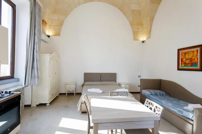 Une piece lumineuse avec un lit, un canape et une kitchenette.
