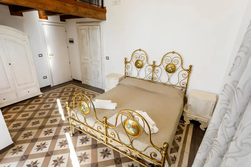 Une chambre lumineuse avec un lit en fer forgé et un sol carrelé.