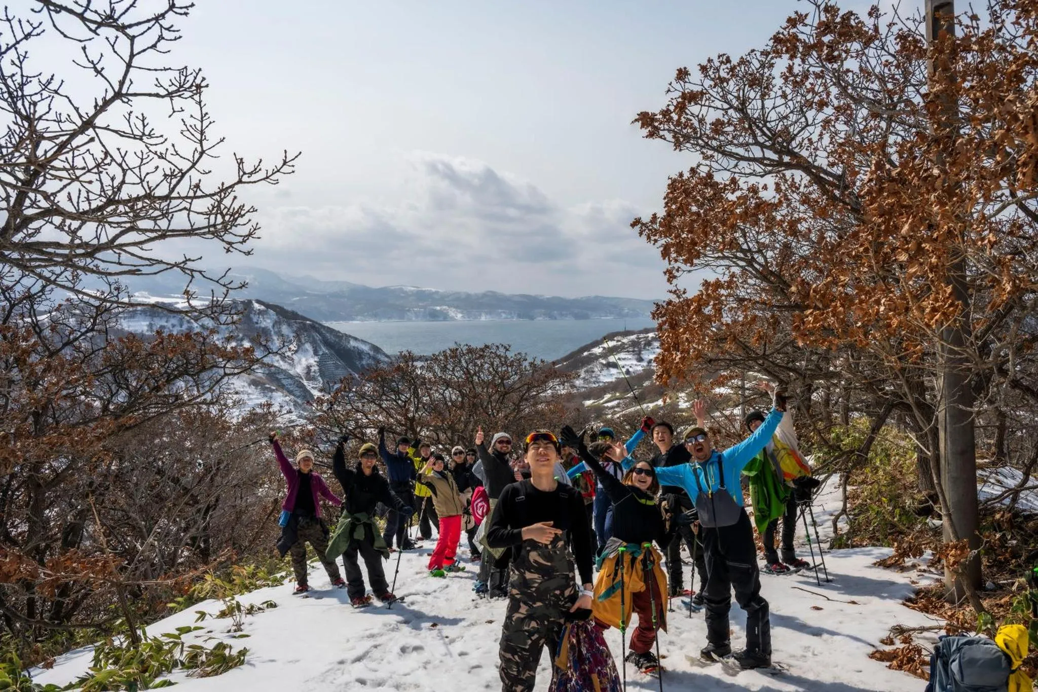 Un groupe de personnes se tient sur une colline enneigée avec une vue sur la mer et les montagnes.