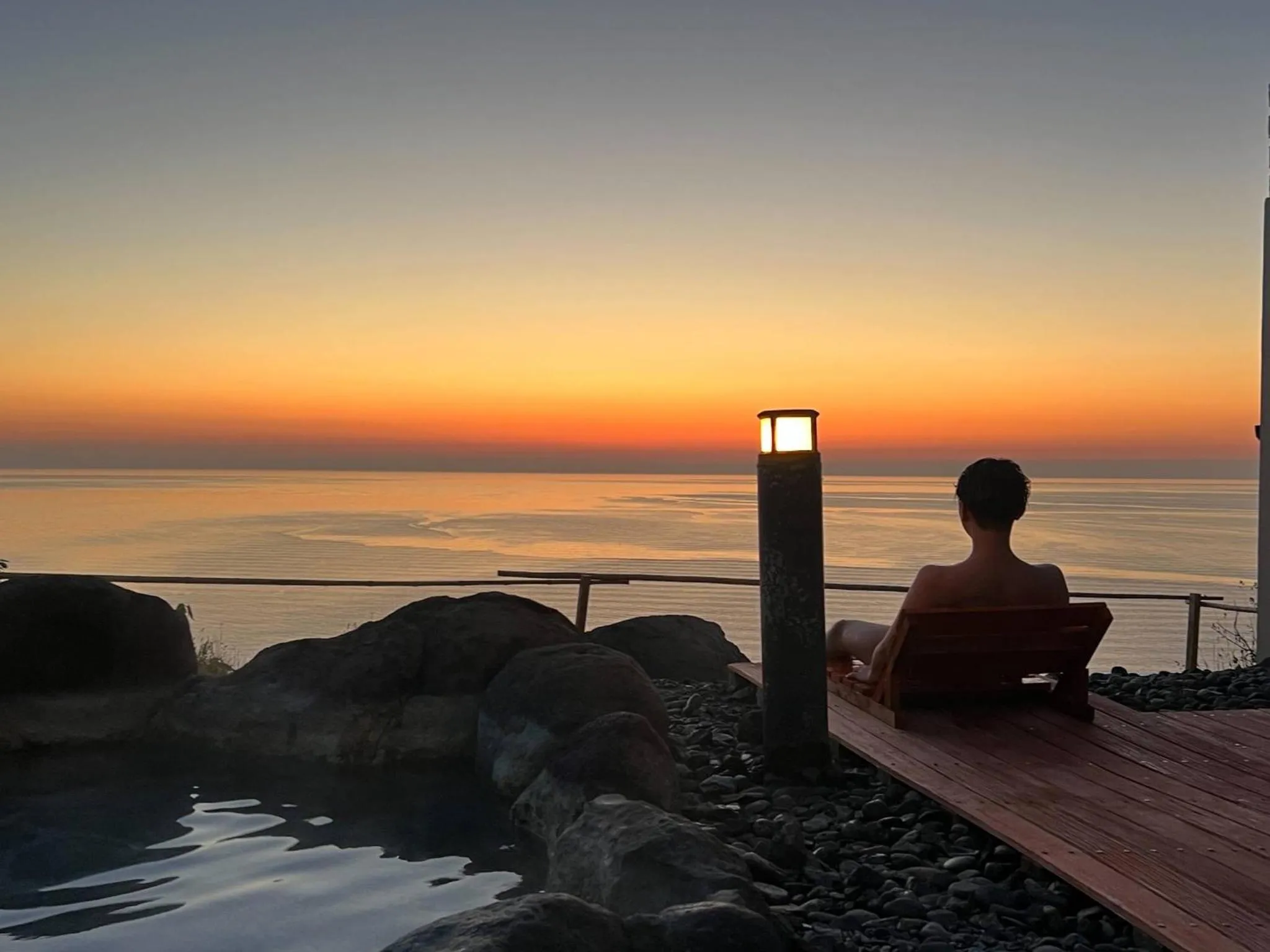 Une personne est assise face à la mer au coucher du soleil.