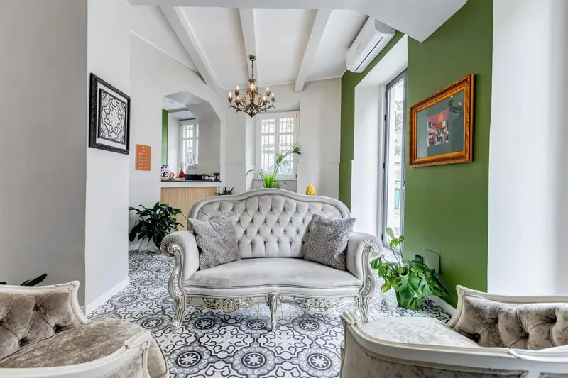Un canapé gris clair est placé dans un hall d'entrée décoré de plantes et de tableaux.