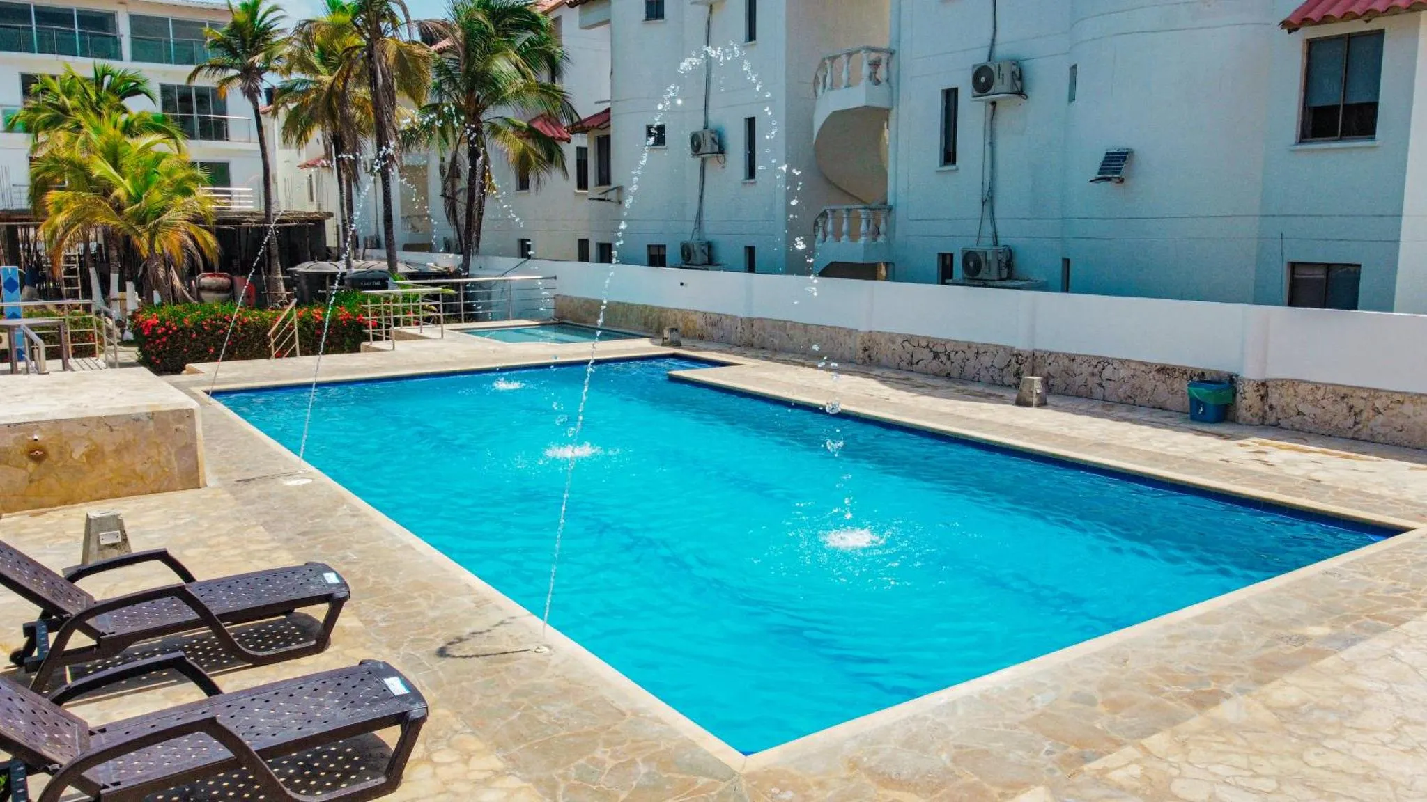 Une piscine rectangulaire avec des jets d'eau et des transats.
