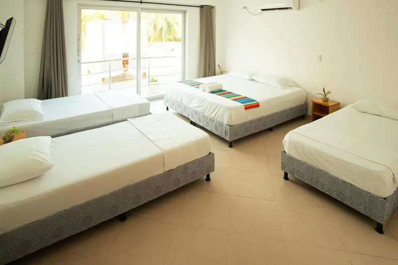Chambre lumineuse avec plusieurs lits simples et vue sur l'extérieur.
