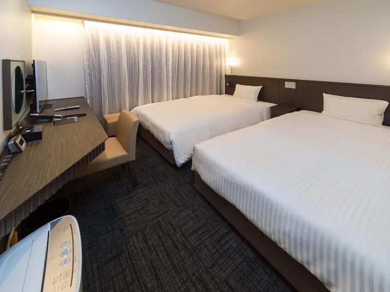 Une chambre d'hôtel lumineuse avec deux lits simples et un bureau.