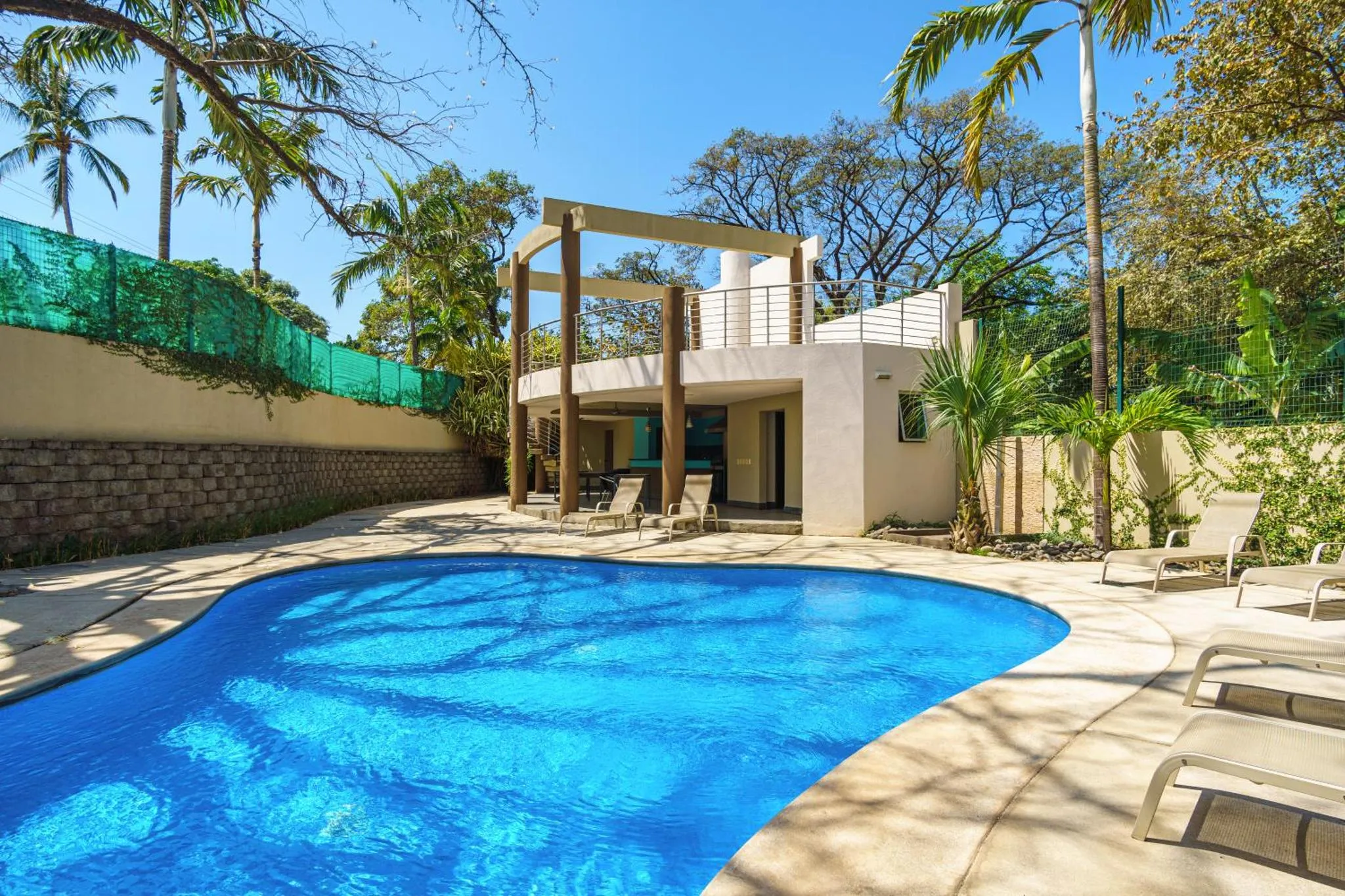 Une piscine bleue bordée de chaises longues devant un bâtiment beige et blanc.