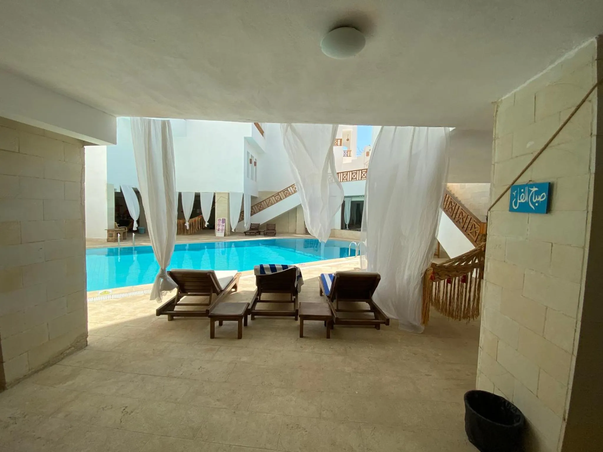 Transats alignés au bord d'une piscine rectangulaire dans un espace ombragé.