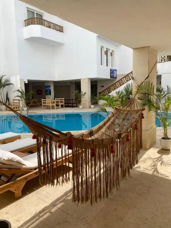 Un hamac tisse se balance devant une piscine et un batiment blanc.