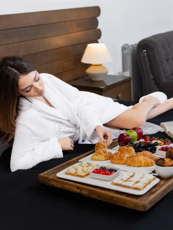 Une femme est assise sur un lit avec un plateau de nourriture.