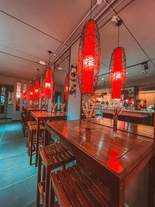 Une salle lumineuse avec des tables en bois et des suspensions rouges.