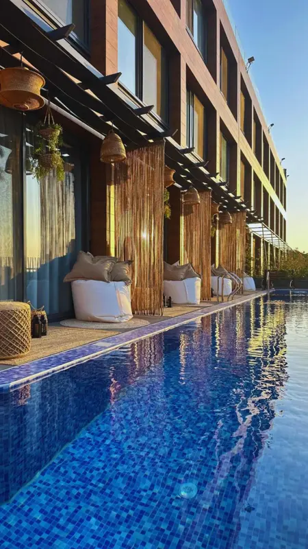 Une piscine rectangulaire bordée de fauteuils blancs et de parasols en osier.
