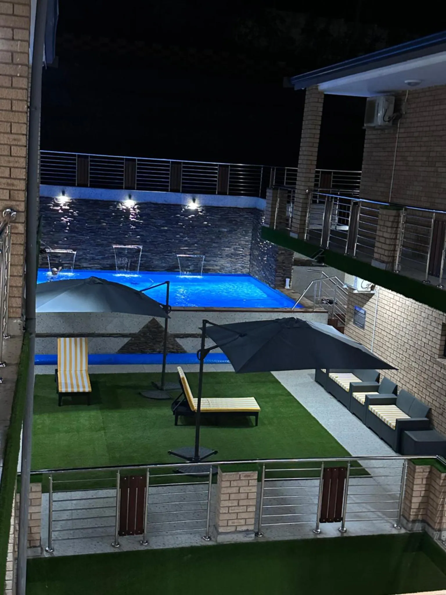 Une piscine illuminée avec des transats et des parasols dans un espace extérieur aménagé.