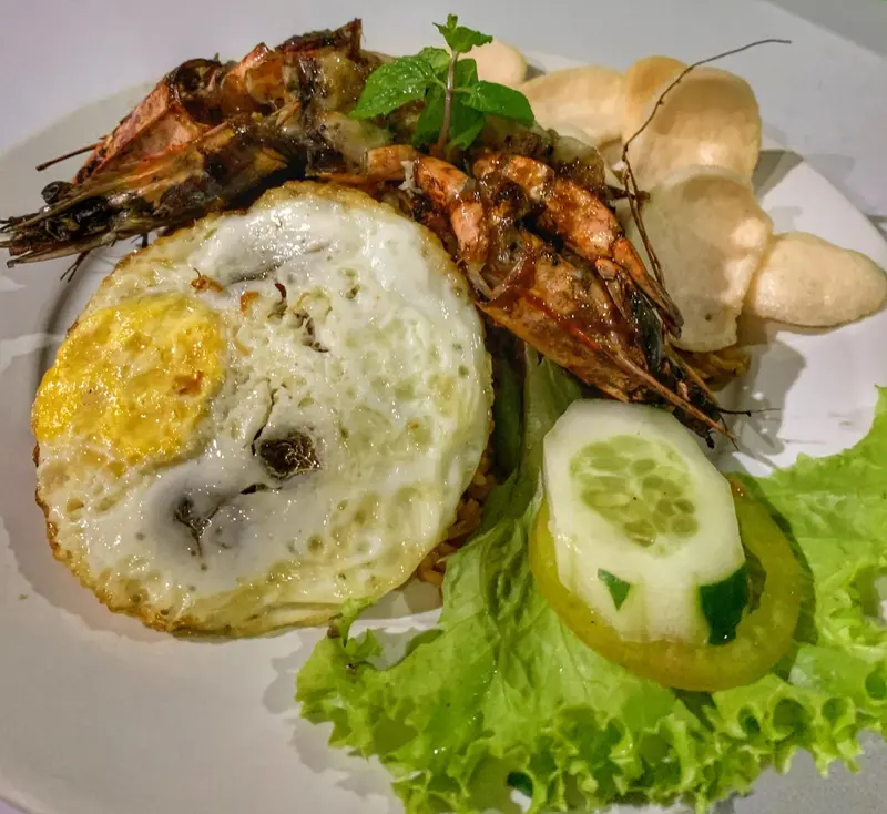 Assiette de crevettes grillées accompagnées d'un œuf au plat et de crudités.