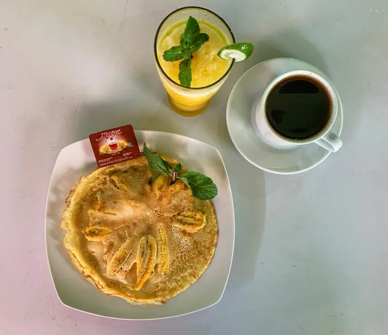 Une assiette présente une crêpe garnie de fruits et accompagnée de boissons.