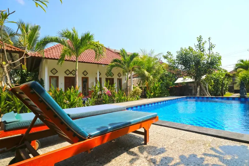 Transats bleus au bord d'une piscine rectangulaire dans un jardin tropical.