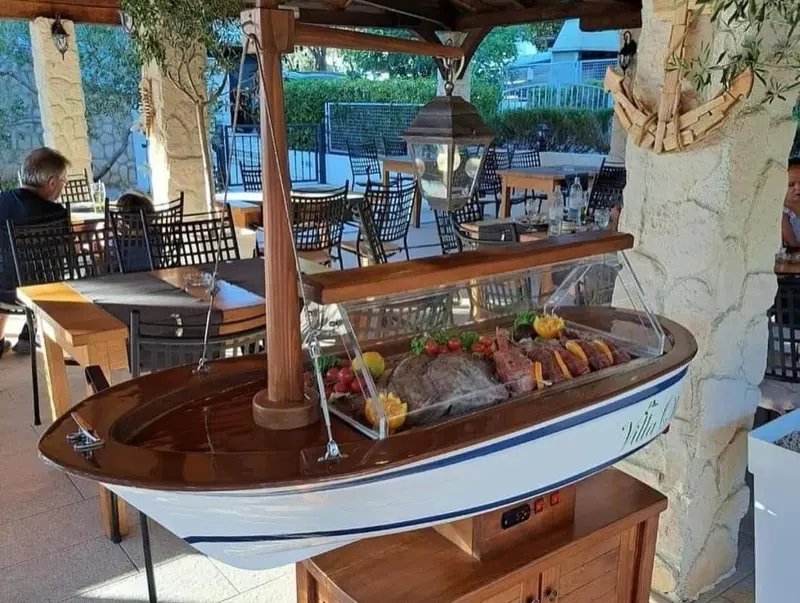 Une terrasse ombragée présente des tables et un buffet de nourriture présenté dans un bateau en bois.